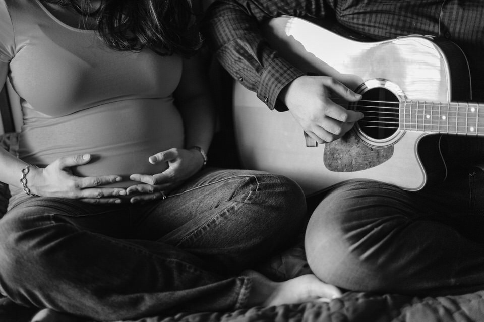 Close up of pregnant woman's belly and husband hands playing guitar