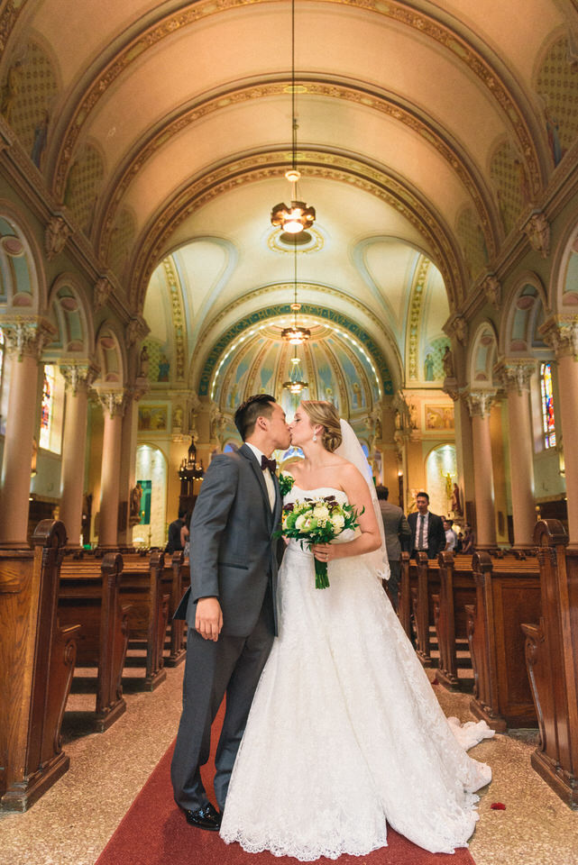 Bride and groom kiss as they walk back the aisle of a Catholic church in Lachine
