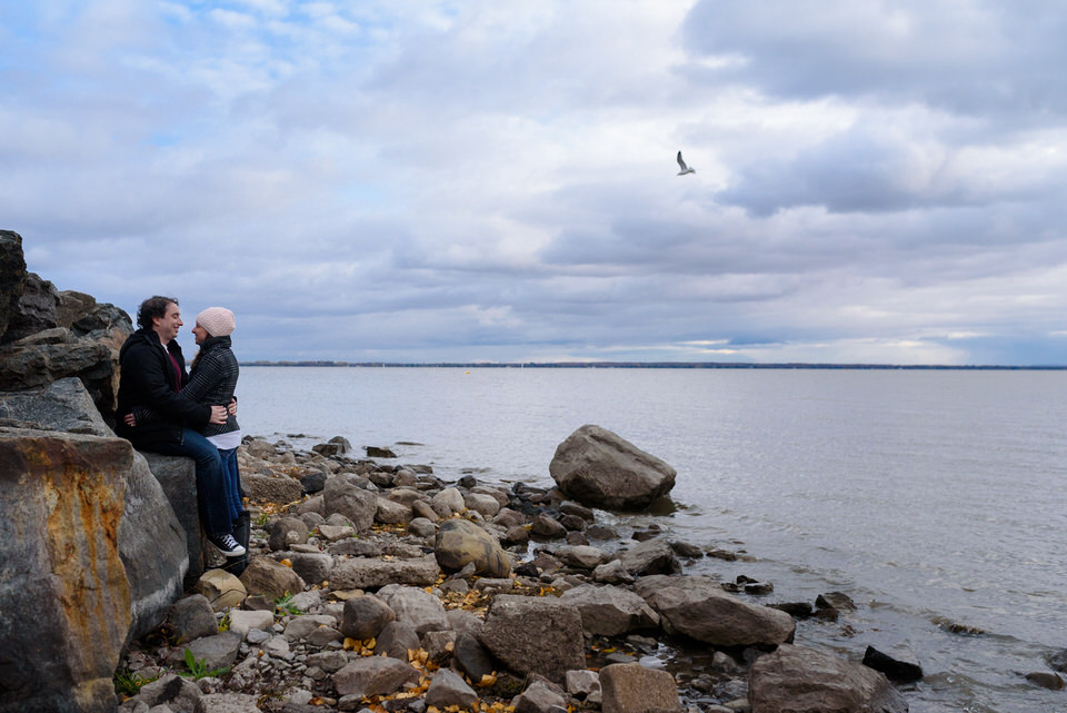 Guy sitting on rocks, holding fiancée near the river