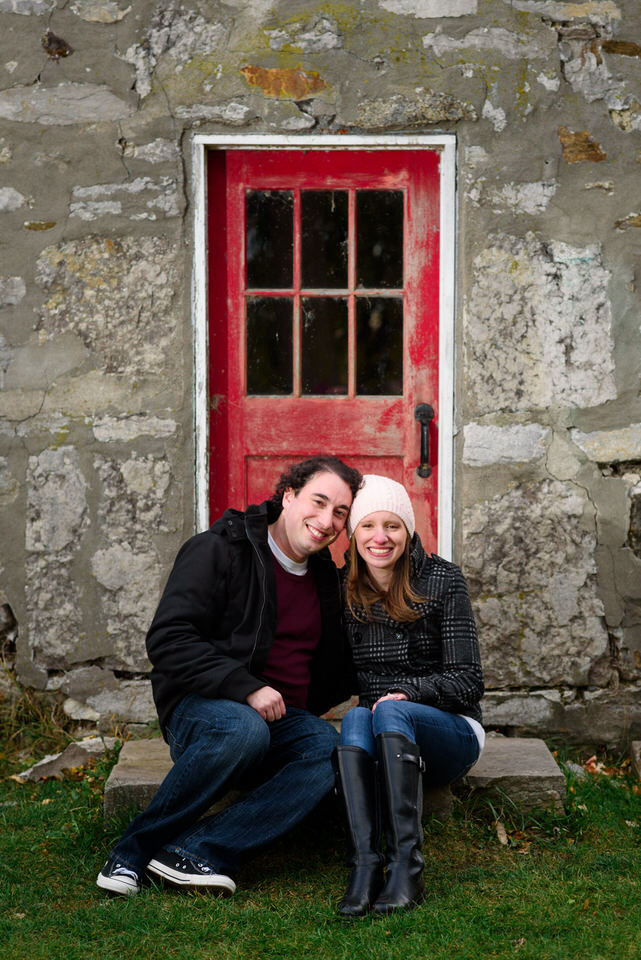 Engaged couple sitting and posing in front Pointe-Claire windmill door