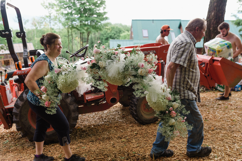 Man and woman carrying an arch of wedding flowers up the hill past a tractor