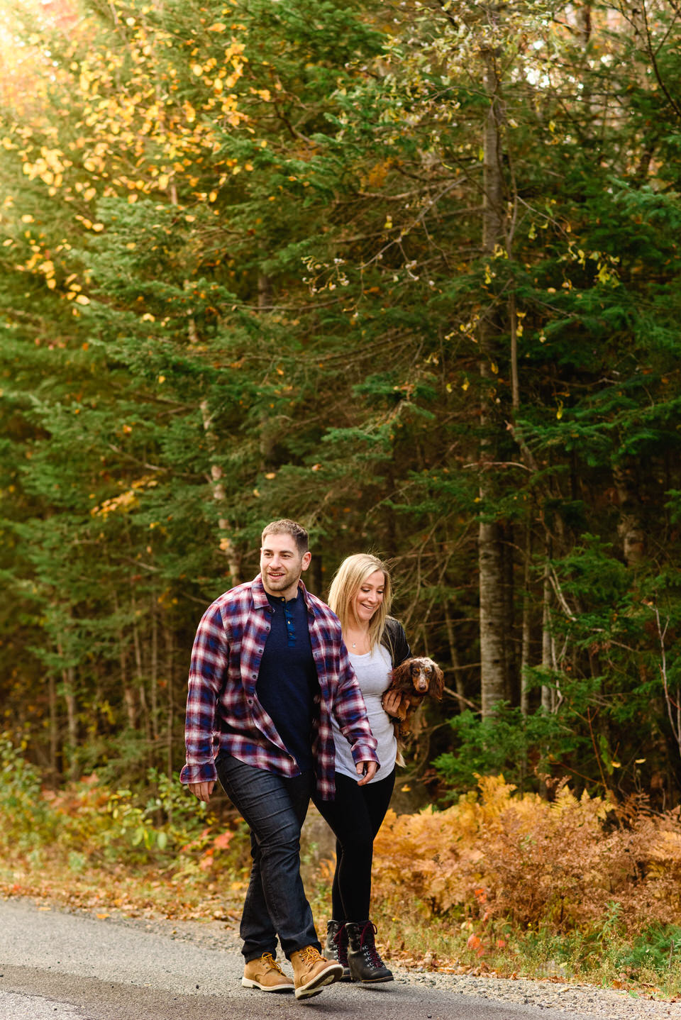 Engaged couple walking in the woods carrying their puppy