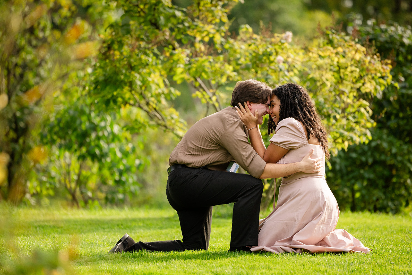 Emotional proposal moments where man is kneeling and woman is kneeling too as she holds his face in her hands